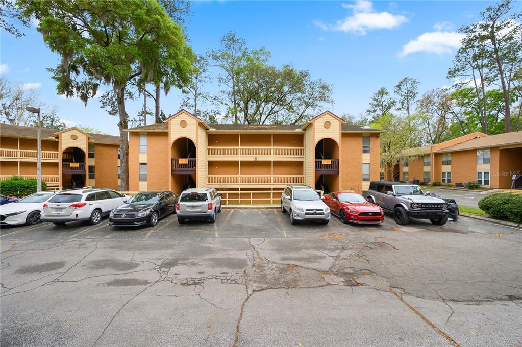 A multi-story apartment building with tan stucco siding and a parking lot in front — 1810 NW 23RD BOULEVARD UNIT 174, GAINESVILLE, FL