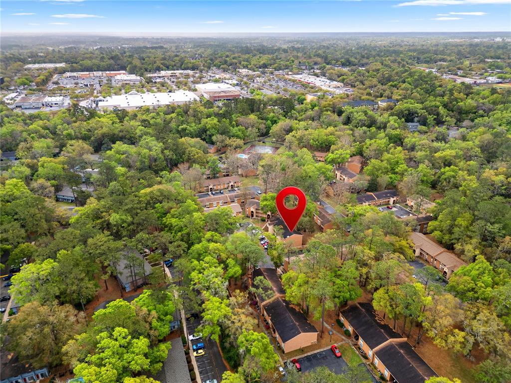 An aerial view shows a multi-unit apartment complex surrounded by dense trees and parking lots — 1810 NW 23RD BOULEVARD UNIT 174, GAINESVILLE, FL