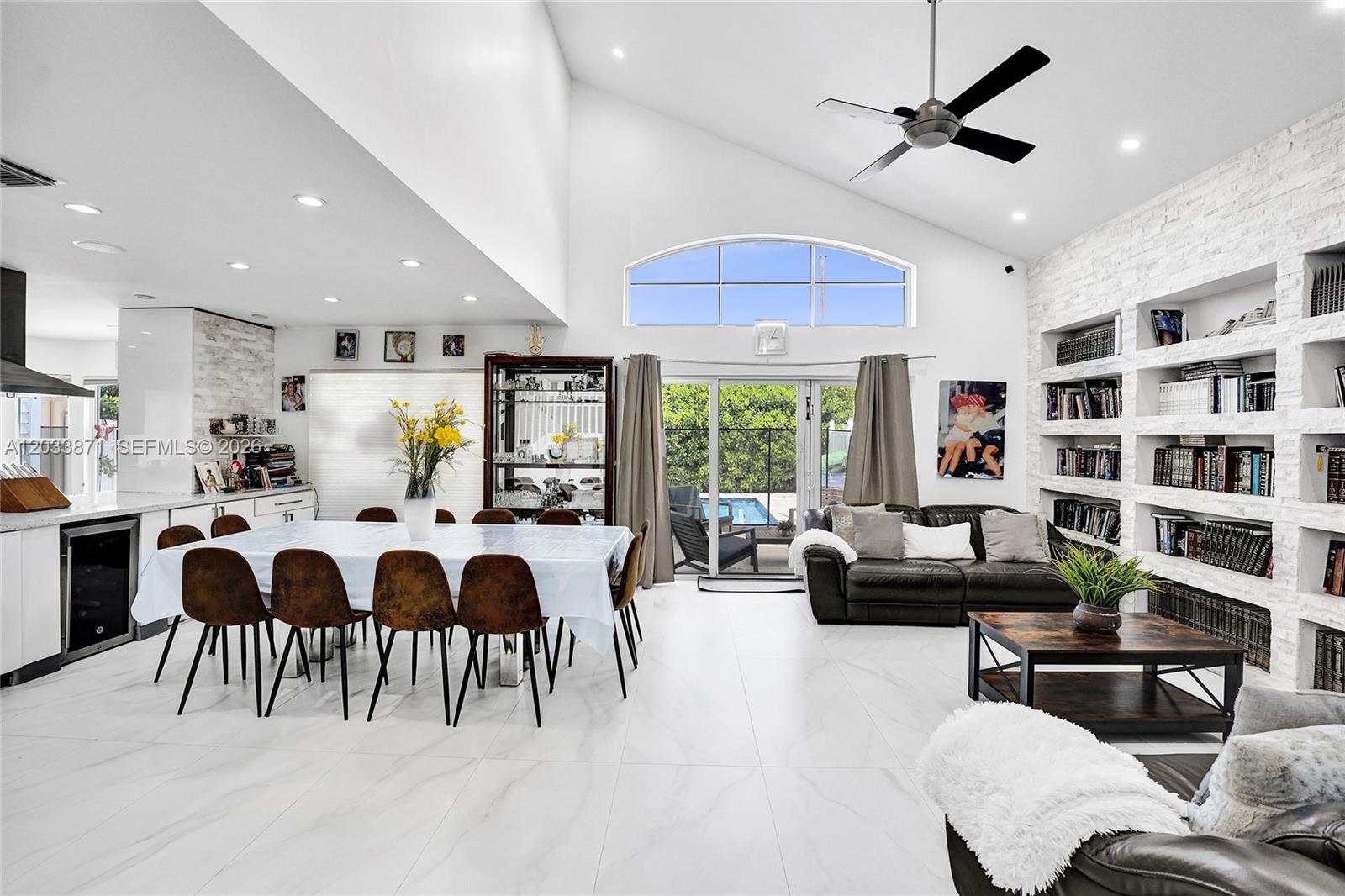 A bright, open-concept living and dining area features vaulted ceilings, white tile floors, and bookshelves — 5080 SW 34th Ter, Hollywood FL 33312, HOLLYWOOD, FL