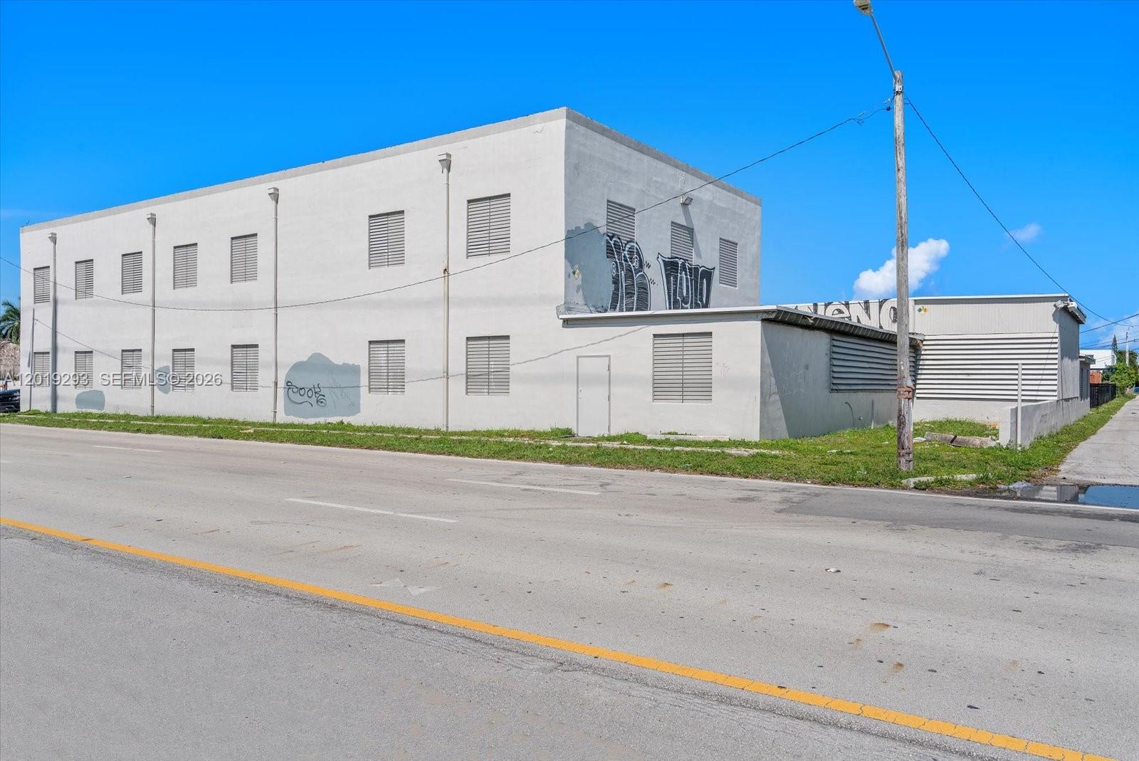 A two-story industrial building with exterior graffiti stands along a paved road under a blue sky — 2040 Liberty St, Hollywood FL 33020, HOLLYWOOD, FL