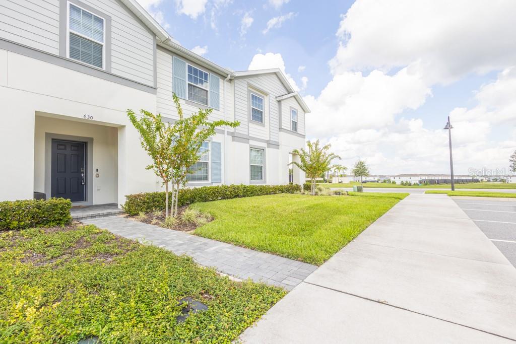 A two-story townhouse exterior features a dark front door, light siding, and a paved walkway — 630 JASMINE LANE, DAVENPORT, FL