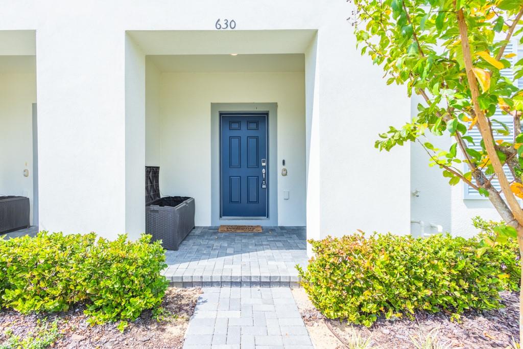 A blue front door is set within a white recessed entryway with a paved walkway — 630 JASMINE LANE, DAVENPORT, FL