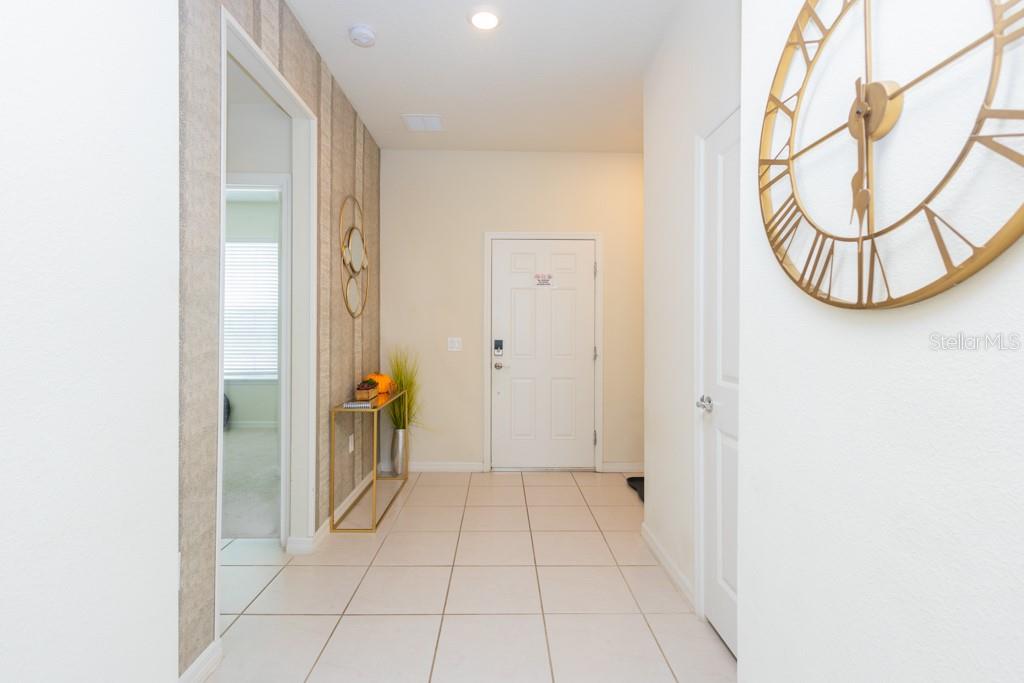 A tiled entryway features a gold console table, wall clock, and a textured accent wall — 630 JASMINE LANE, DAVENPORT, FL