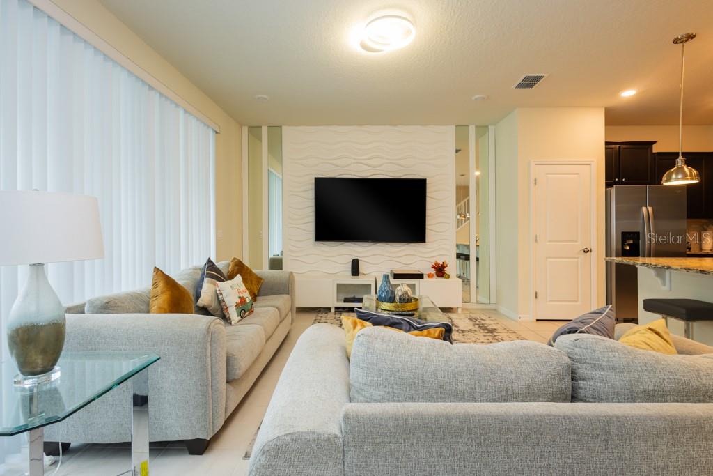 A living room features a textured white accent wall with a mounted television and sofas — 630 JASMINE LANE, DAVENPORT, FL