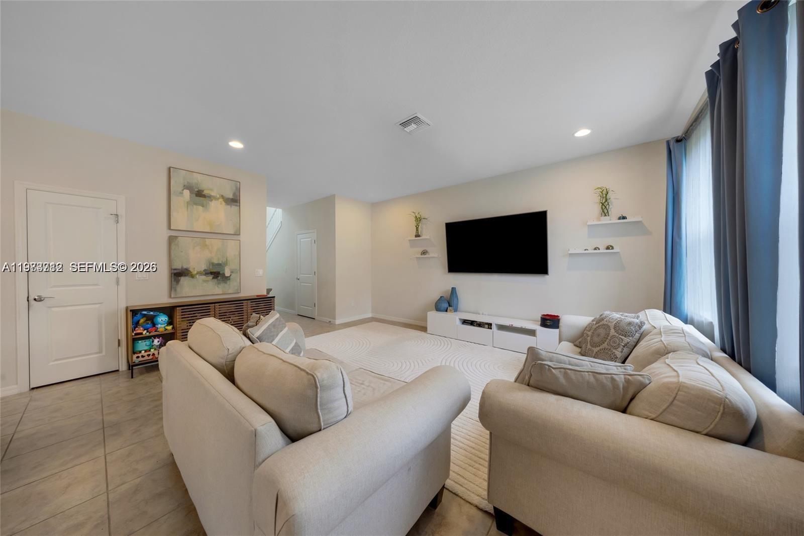 A living room features two beige sofas, a wall-mounted television, and light-colored tile flooring — 932 Banyan Dr, Hollywood FL 33021, HOLLYWOOD, FL