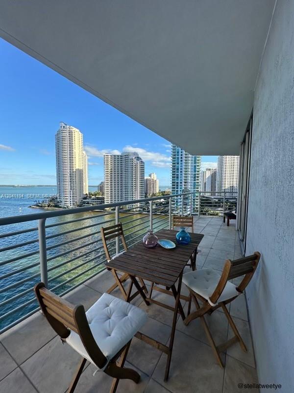 A balcony with a wooden table and chairs overlooks a bay and city skyline — 325 S Biscayne Blvd # 1523, Miami FL 33131, MIAMI, FL