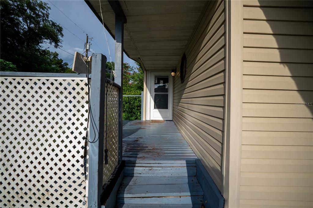 A wooden porch with a lattice privacy screen leads to a white exterior door — 4010 SE 138TH PLACE, SUMMERFIELD, FL