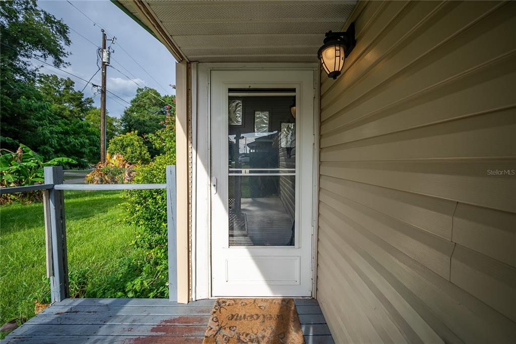 A white storm door leads to a porch with light-colored siding and a welcome mat — 4010 SE 138TH PLACE, SUMMERFIELD, FL
