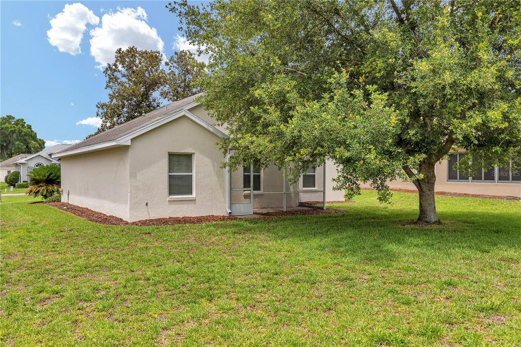 The exterior of a beige house features a screened-in patio and a large shade tree — 7296 SW 112TH PLACE, OCALA, FL