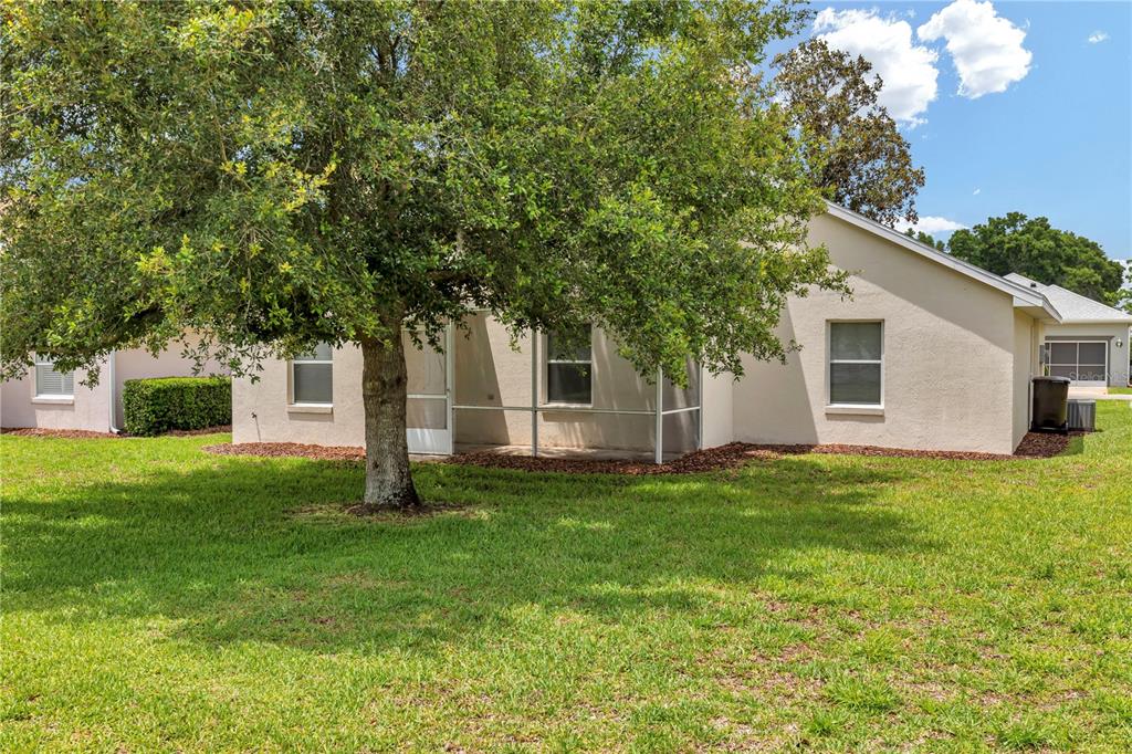 The exterior of a beige house features a screened-in patio and a large shade tree — 7296 SW 112TH PLACE, OCALA, FL