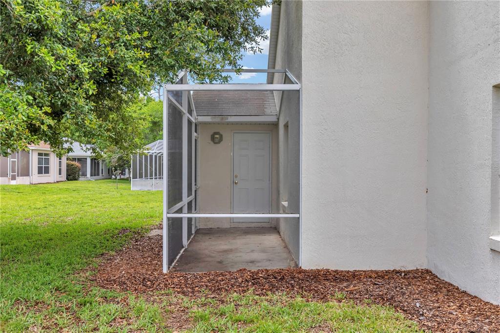 A screened-in entryway with a white door sits beside a stucco exterior wall — 7296 SW 112TH PLACE, OCALA, FL
