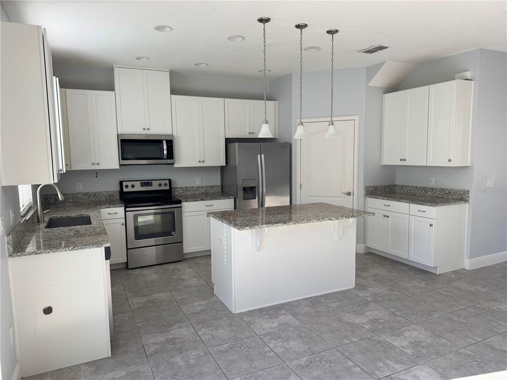 A kitchen features white cabinets, granite countertops, stainless steel appliances, and a central island — 13963 ARCLID STREET, ORLANDO, FL