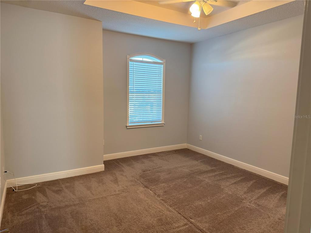 An empty bedroom with gray carpet, light walls, a tray ceiling, and an arched window — 13963 ARCLID STREET, ORLANDO, FL