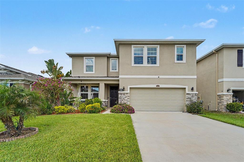 A two-story suburban house features a beige stucco exterior, stone accents, and a two-car garage — 3221 LIVING CORAL DRIVE, ODESSA, FL