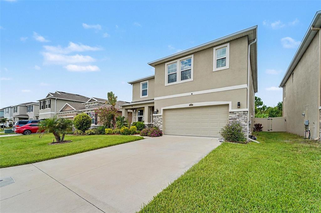 A two-story suburban house with a beige stucco exterior, stone accents, and a concrete driveway — 3221 LIVING CORAL DRIVE, ODESSA, FL