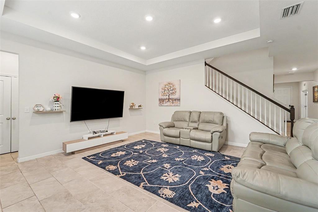 A living room features a tray ceiling, tile flooring, a large area rug, and a staircase — 3221 LIVING CORAL DRIVE, ODESSA, FL