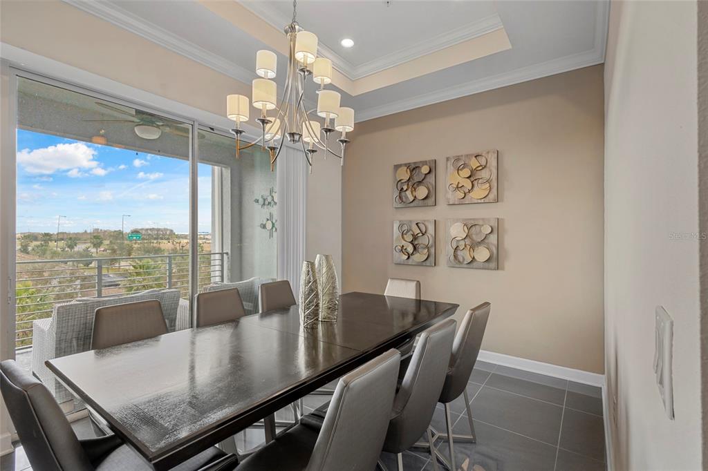 A dining room features a dark wood table, gray chairs, a chandelier, and balcony views — 4751 CLOCK TOWER DRIVE UNIT 402, KISSIMMEE, FL