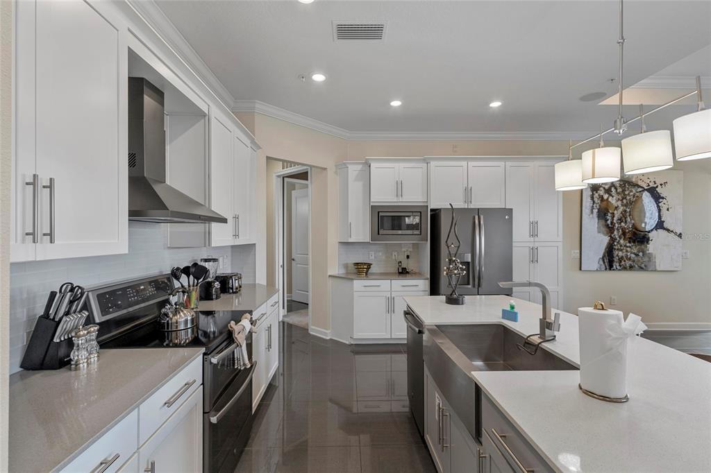A modern kitchen features white cabinetry, stainless steel appliances, a large island, and gray flooring — 4751 CLOCK TOWER DRIVE UNIT 402, KISSIMMEE, FL