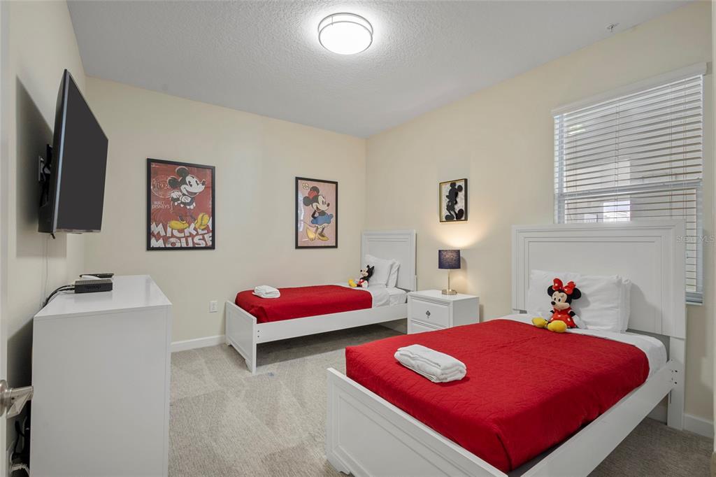 A bedroom features two twin beds with red bedding, white frames, and Disney-themed wall art — 4751 CLOCK TOWER DRIVE UNIT 402, KISSIMMEE, FL