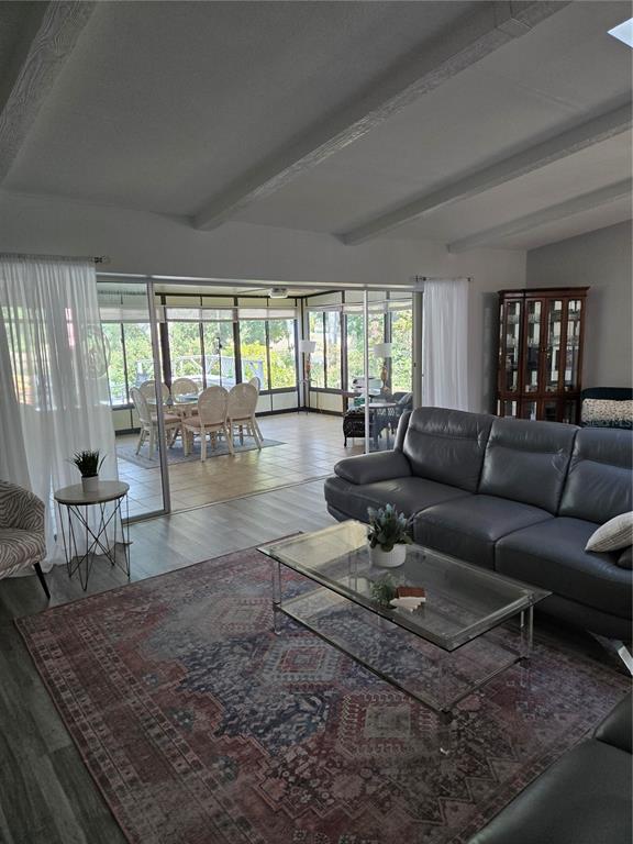 A living room with a grey sofa and area rug opens to a sunroom with dining — 3235 BUCKHORN DRIVE, CLEARWATER, FL