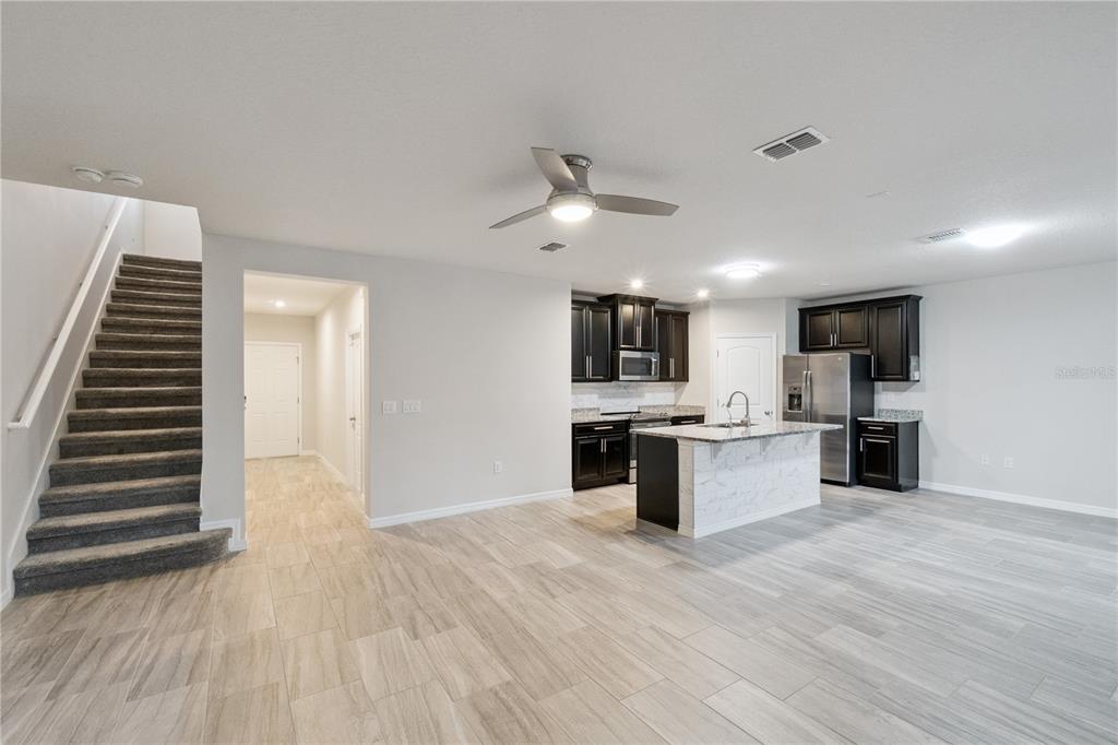 An open-concept kitchen with dark cabinets and a marble-topped island sits beside a carpeted staircase — 4406 SILVER CREEK STREET, KISSIMMEE, FL