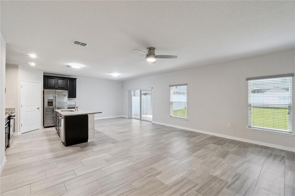 An open-concept kitchen and living area with light tile flooring, dark cabinets, and sliding doors — 4406 SILVER CREEK STREET, KISSIMMEE, FL