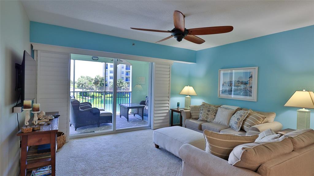 A living room with light blue walls, a ceiling fan, and a sliding door to a balcony — 5300 S ATLANTIC AVENUE UNIT 15-202, NEW SMYRNA BEACH, FL