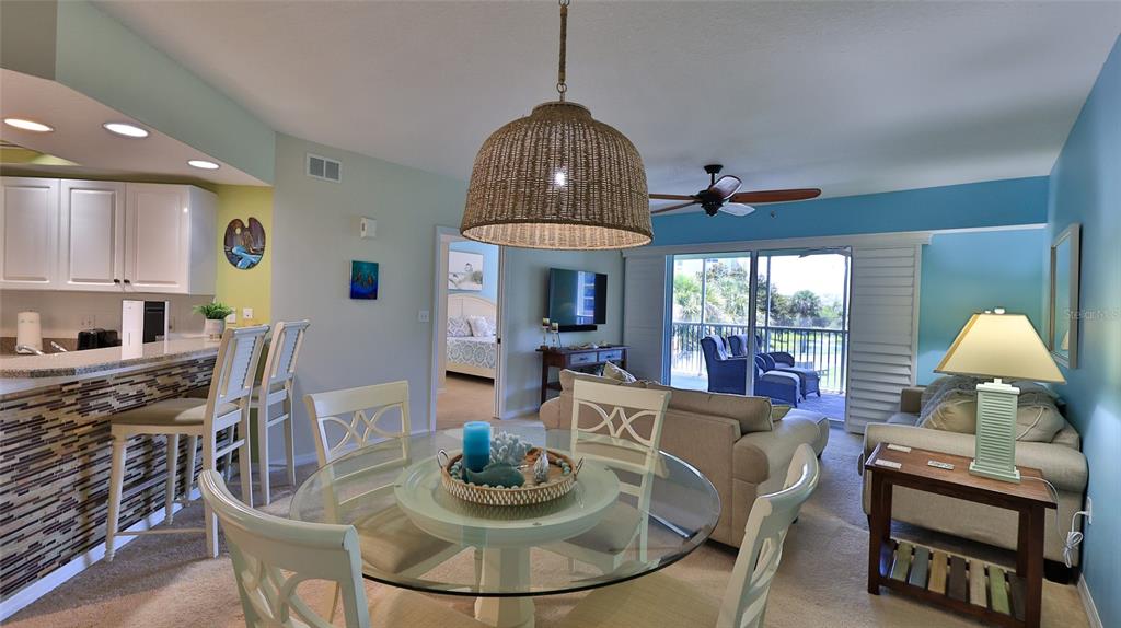 A dining area with a glass table and wicker pendant light opens to a living room — 5300 S ATLANTIC AVENUE UNIT 15-202, NEW SMYRNA BEACH, FL