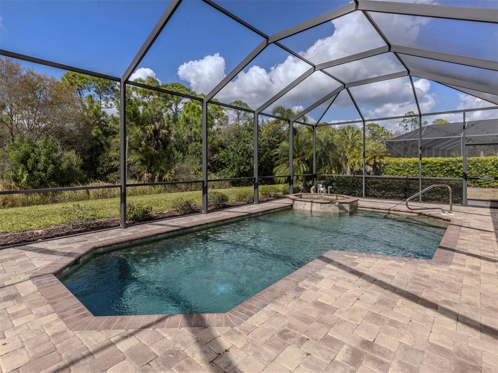 A screened-in swimming pool and spa with a brick paver deck overlooking a wooded area — 20925 LOGGIA COURT, VENICE, FL