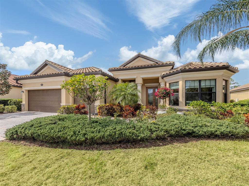 A single-story tan stucco house with a tile roof, two-car garage, and landscaped front yard — 20925 LOGGIA COURT, VENICE, FL