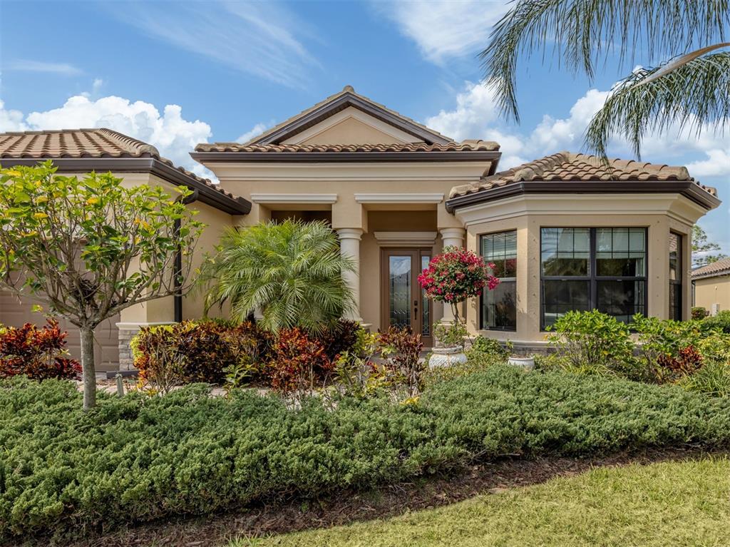 The exterior of a beige, single-story house features a tiled roof, columns, and landscaped gardens — 20925 LOGGIA COURT, VENICE, FL