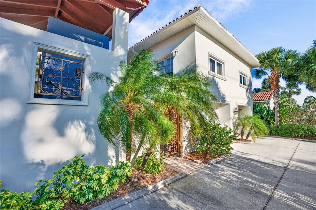 A two-story stucco house features a palm tree, a decorative metal gate, and a driveway — 831 MANDALAY AVENUE, CLEARWATER BEACH, FL