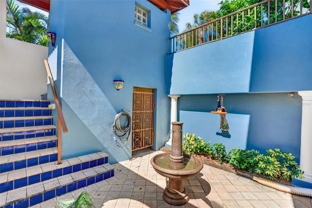 A blue exterior courtyard features a stone fountain, tiled stairs, and a decorative metal door — 831 MANDALAY AVENUE, CLEARWATER BEACH, FL