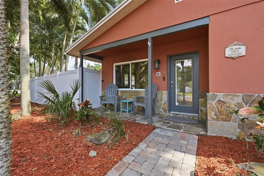 A front porch with stone veneer, two chairs, and a brick walkway leads to a gray door — 961 LEXINGTON DRIVE, DUNEDIN, FL