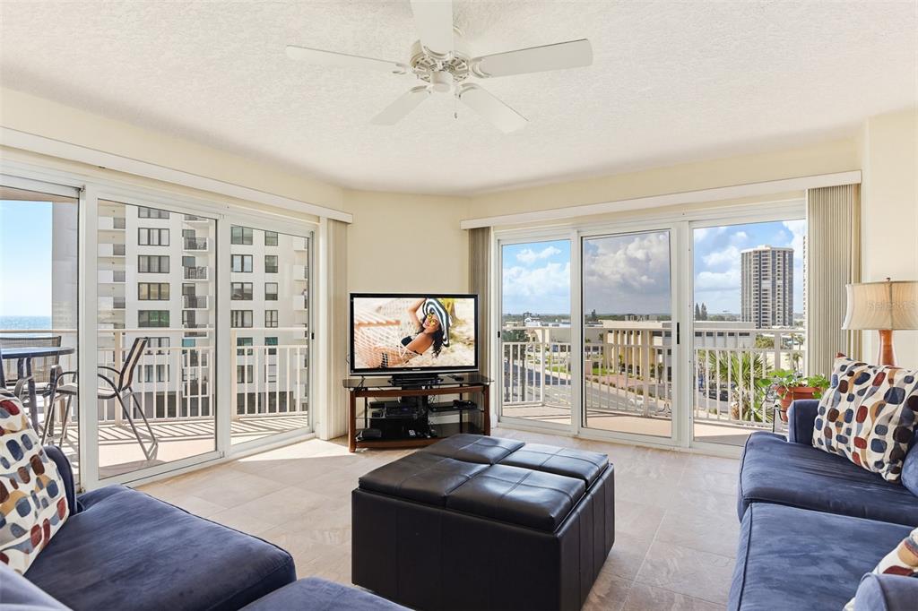 A living room features blue sofas, a leather ottoman, and sliding glass doors with balcony views — 2967 S ATLANTIC AVENUE UNIT 408, DAYTONA BEACH SHORES, FL