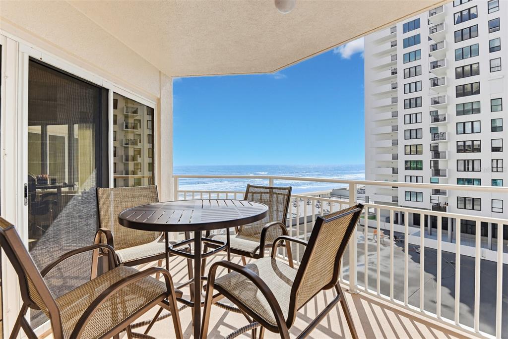 A balcony with a round table and four chairs overlooks the ocean and a building — 2967 S ATLANTIC AVENUE UNIT 408, DAYTONA BEACH SHORES, FL