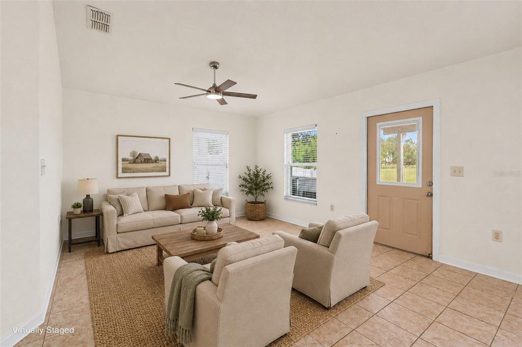 A living room with tile floors, a ceiling fan, and a tan door to the outside — 31331 SATINLEAF RUN, BROOKSVILLE, FL
