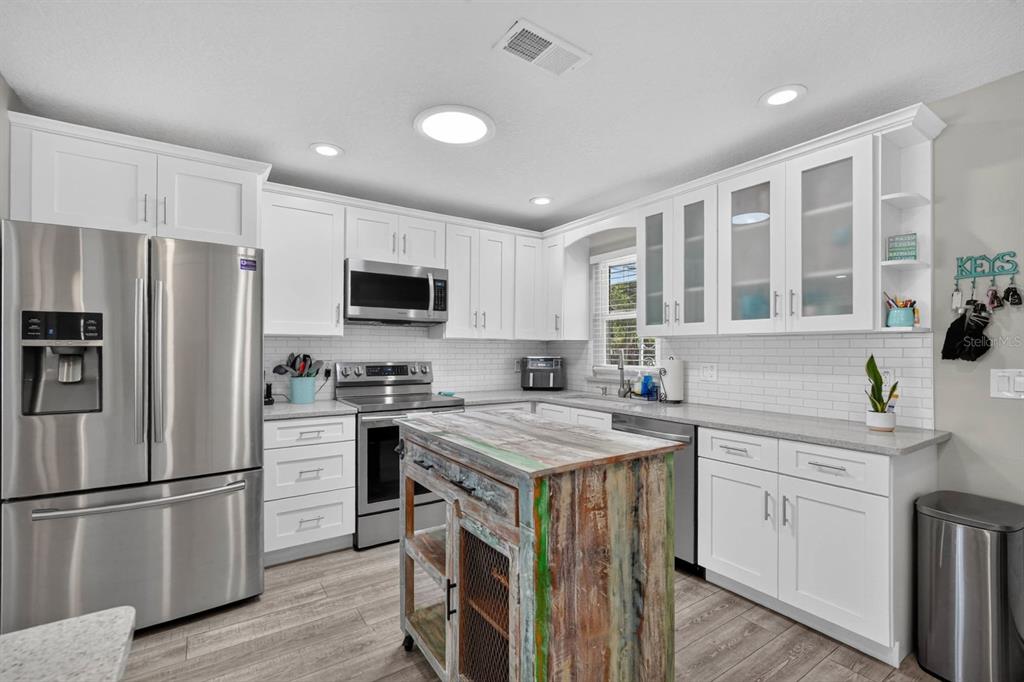 A kitchen with white cabinets, stainless steel appliances, a subway tile backsplash, and a rustic island — 4503 SAXON DRIVE, NEW SMYRNA BEACH, FL