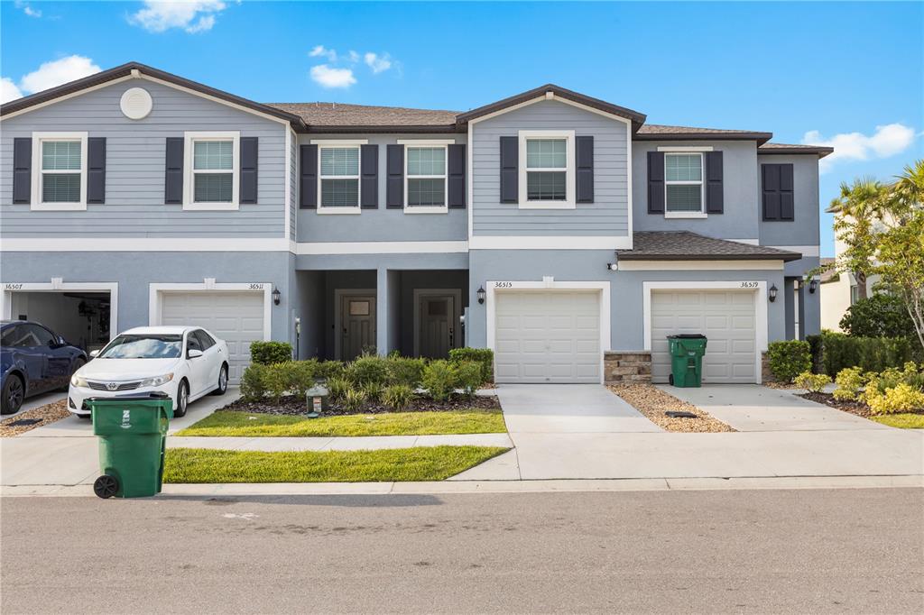 A multi-unit residential building features light blue siding, gray shutters, and four garage doors — 36515 CAMP FIRE TERRACE, ZEPHYRHILLS, FL