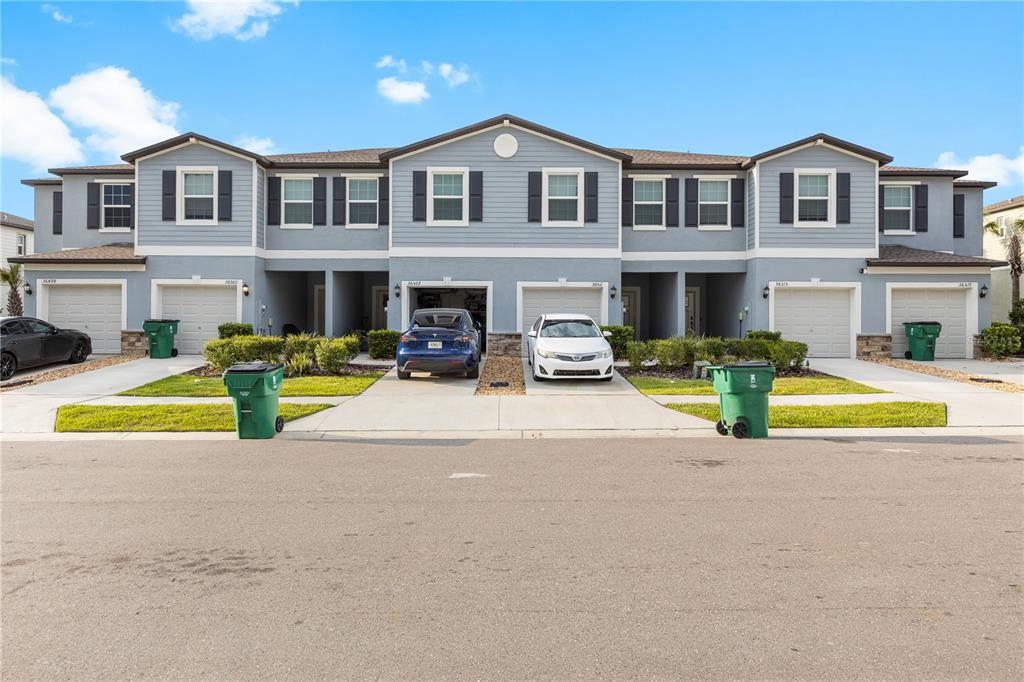A row of two-story townhomes with light blue siding, attached garages, and green trash bins — 36515 CAMP FIRE TERRACE, ZEPHYRHILLS, FL
