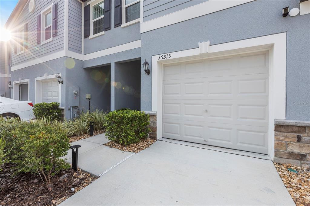 A view of a residential garage exterior with a concrete driveway and small landscaping — 36515 CAMP FIRE TERRACE, ZEPHYRHILLS, FL