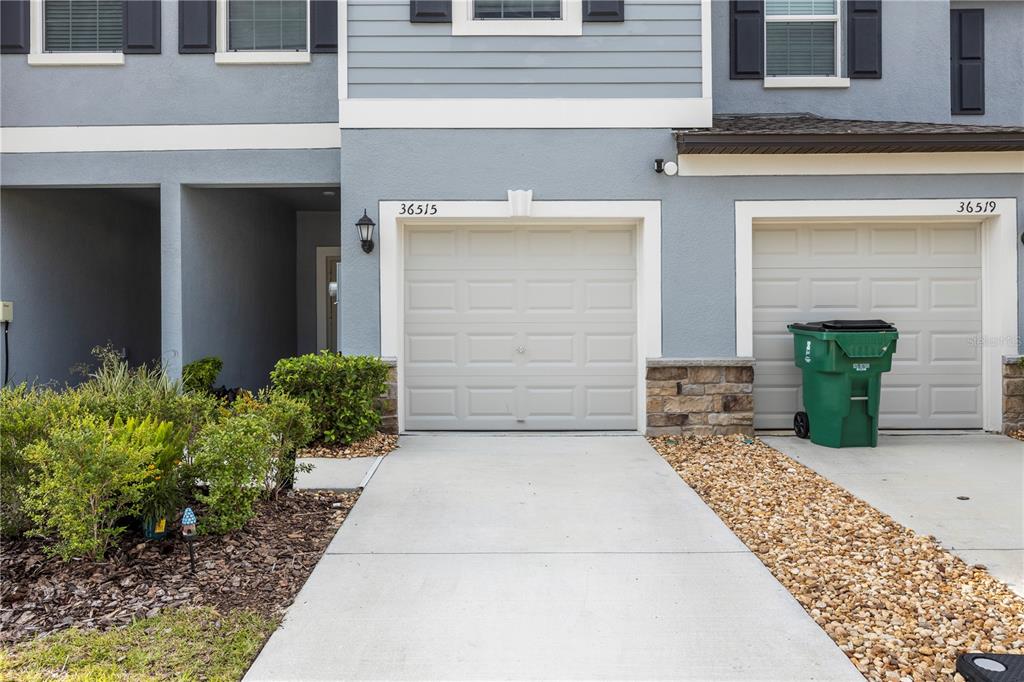 The exterior of a two-story townhouse features two garage doors, a driveway, and landscaping — 36515 CAMP FIRE TERRACE, ZEPHYRHILLS, FL