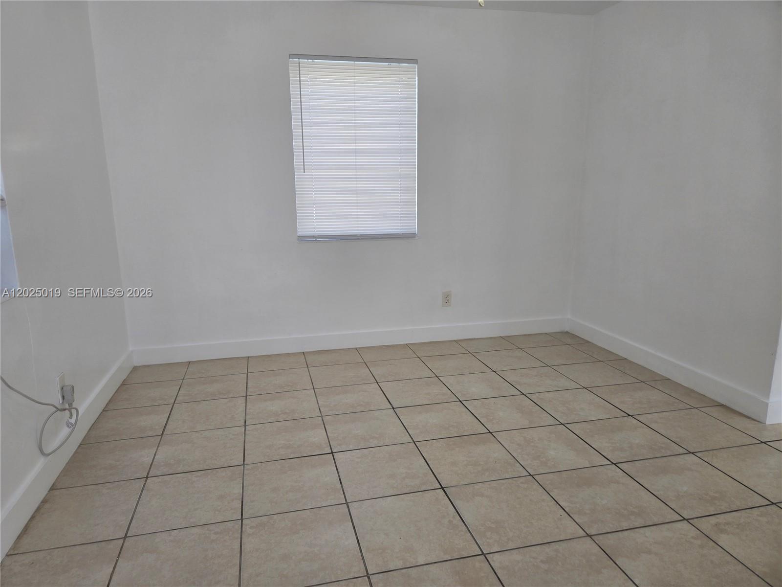 An empty room features white walls, beige tile flooring, and a single window with blinds — 408 NW 8th St # 408, Hallandale Beach FL 33009, HALLANDALE BEACH, FL