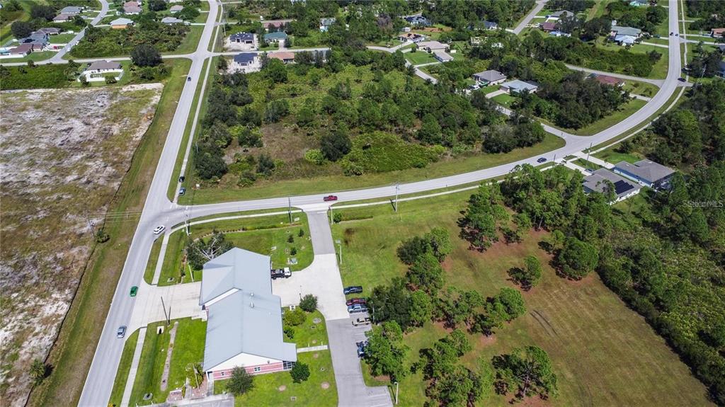 An aerial view shows a commercial building with a parking lot surrounded by wooded residential lots — 1200 N BISCAYNE DRIVE, NORTH PORT, FL