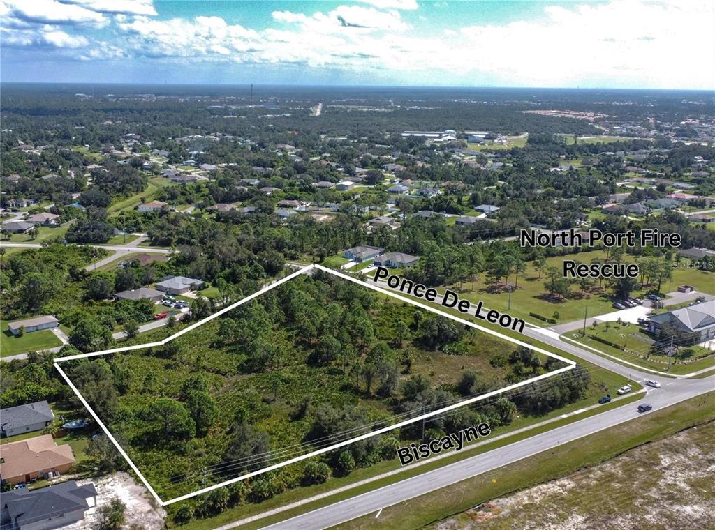 An aerial view shows a vacant, wooded corner lot outlined in white near a road intersection — 1200 N BISCAYNE DRIVE, NORTH PORT, FL