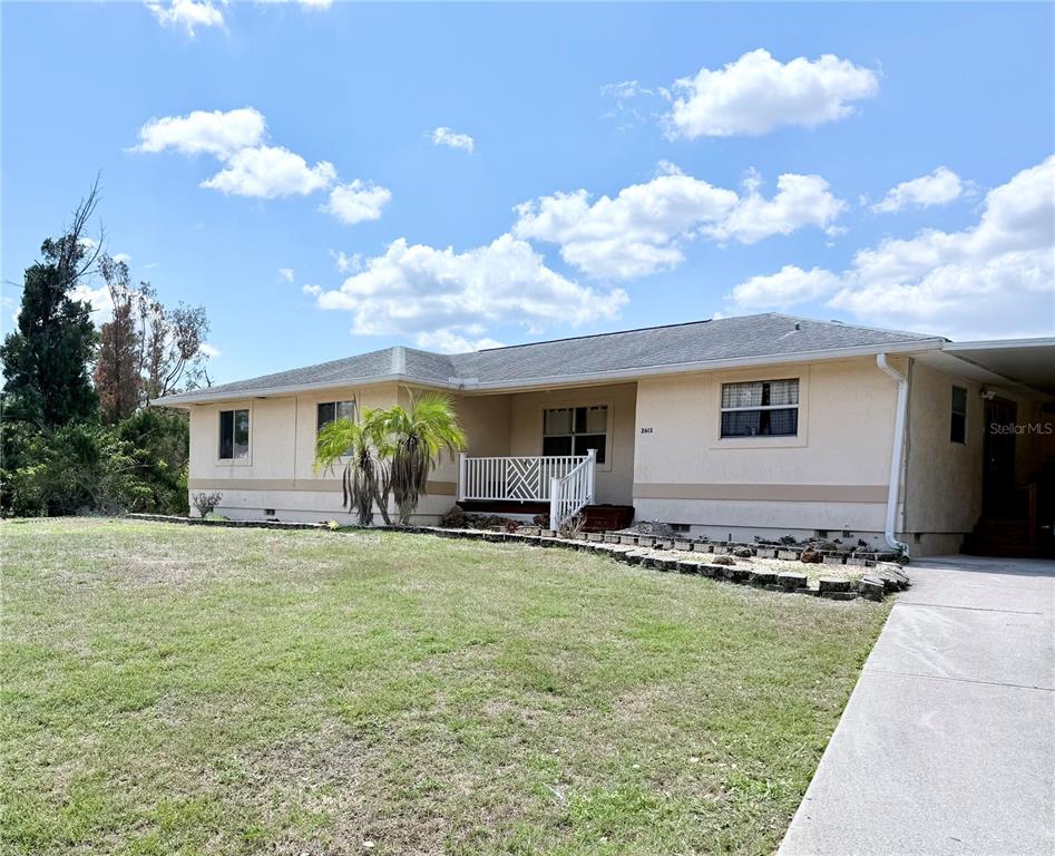 A single-story house with a beige exterior, a covered porch, and a large grassy yard — 2613 VIZZA LANE, NORTH PORT, FL