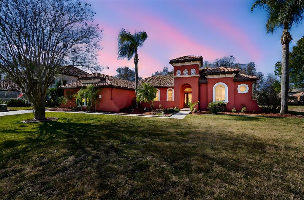 A single-story, red-stucco house with a tile roof and arched windows sits on a lawn — 3511 BALLASTONE DRIVE, LAND O LAKES, FL