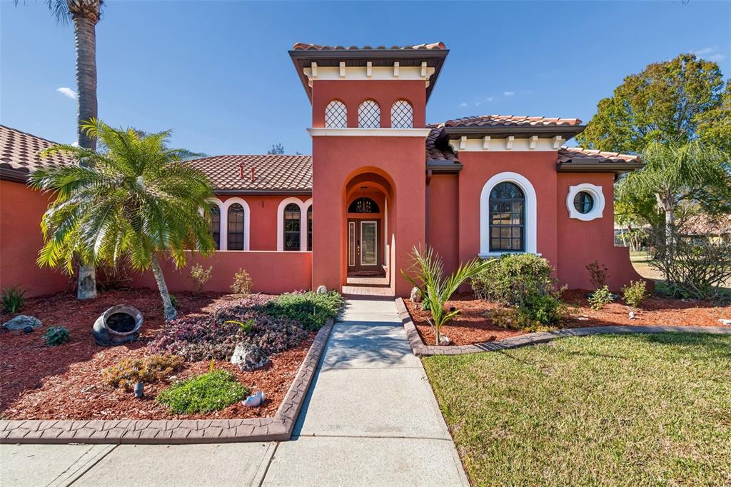 A terracotta-colored house with a central tower, arched entryway, and a palm tree in front — 3511 BALLASTONE DRIVE, LAND O LAKES, FL