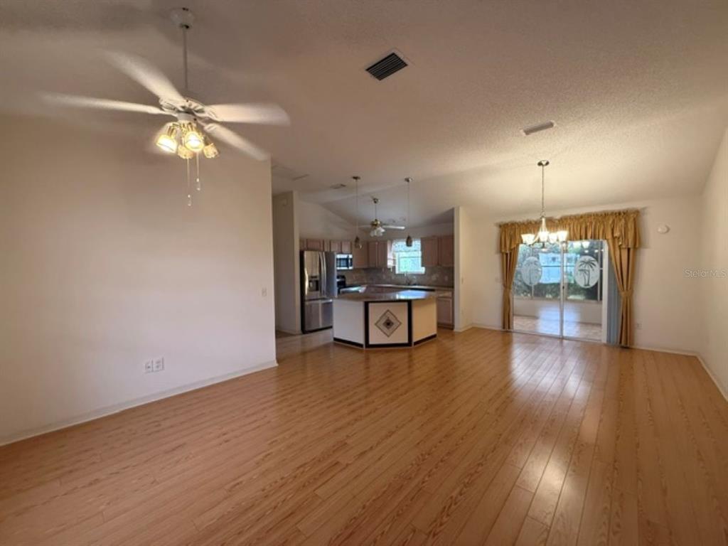 An open-concept living and dining area features light wood flooring and a central kitchen island — 3105 BERWYN WAY, THE VILLAGES, FL