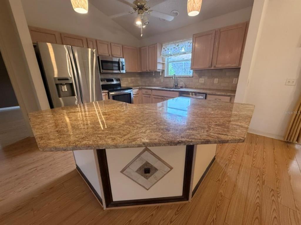 A kitchen features a granite-topped peninsula, light wood cabinets, stainless steel appliances, and wood flooring — 3105 BERWYN WAY, THE VILLAGES, FL